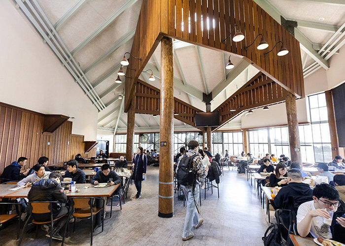 The interior of the main dining room in Foothill Dining Commons. Many students sit at tables on either side of the dining room, and a student wearing a backpack walks back towards the center of the room.