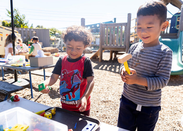 Two young children play with toys on a bench in the children’s outdoor play area.